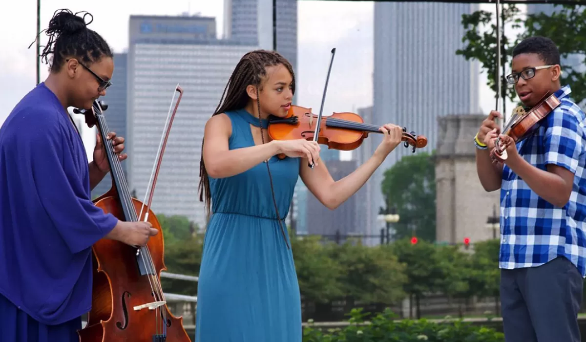 Two young women and one young man in blue playing instruments