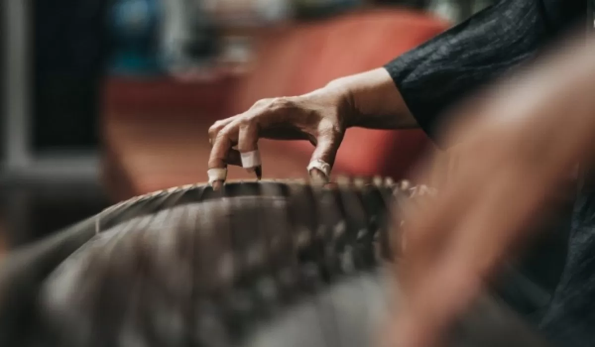 Close-up of a musician’s hand playing a gayageum, a traditional Korean string instrument.