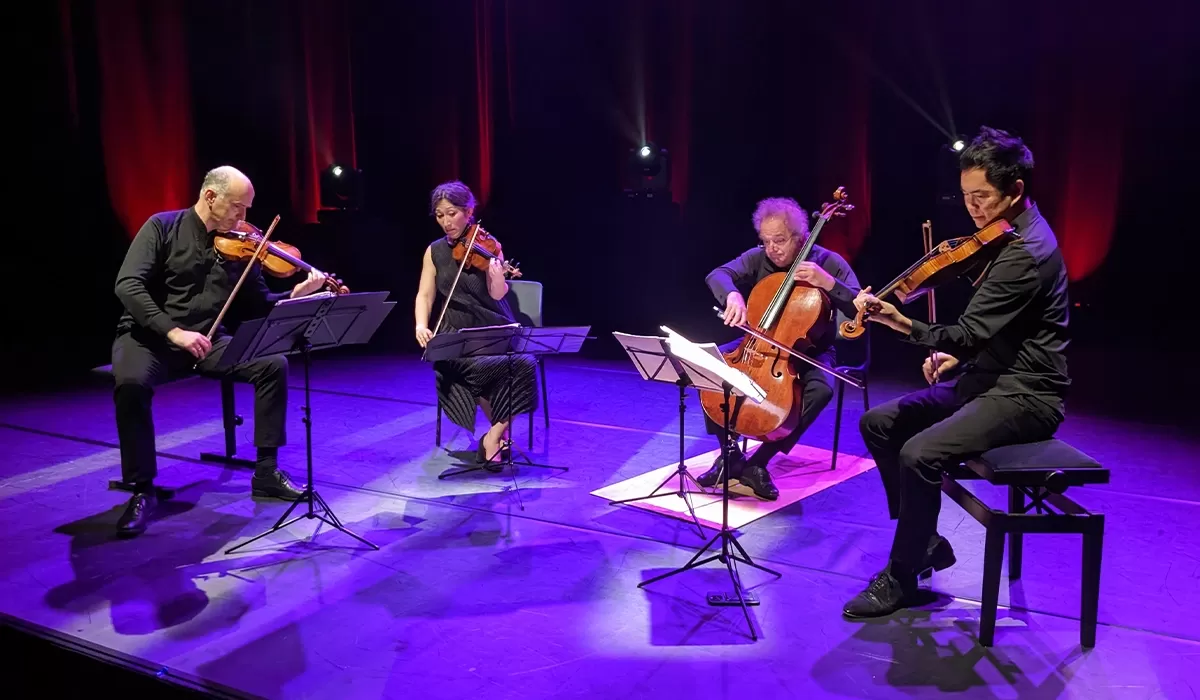 Four stringed instrument players on a purple lit stage.