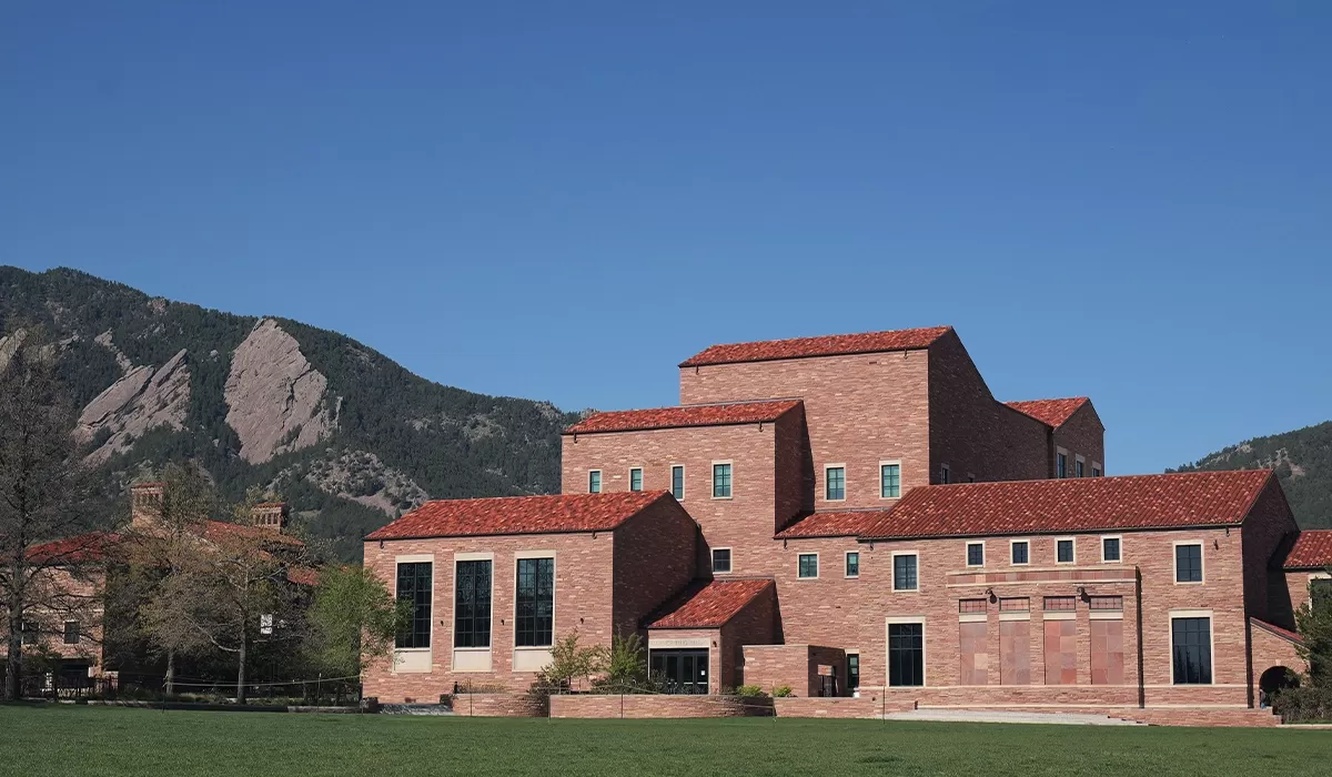 Exterior of the Imig Music Building on the CU Boulder campus, with the Flatirons rising behind it under a clear blue sky.