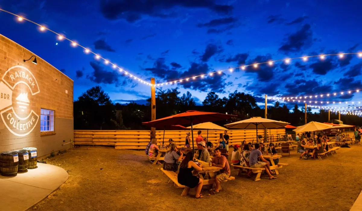 Outdoor garden at dusk with picnic tables, umbrellas, and string lights.