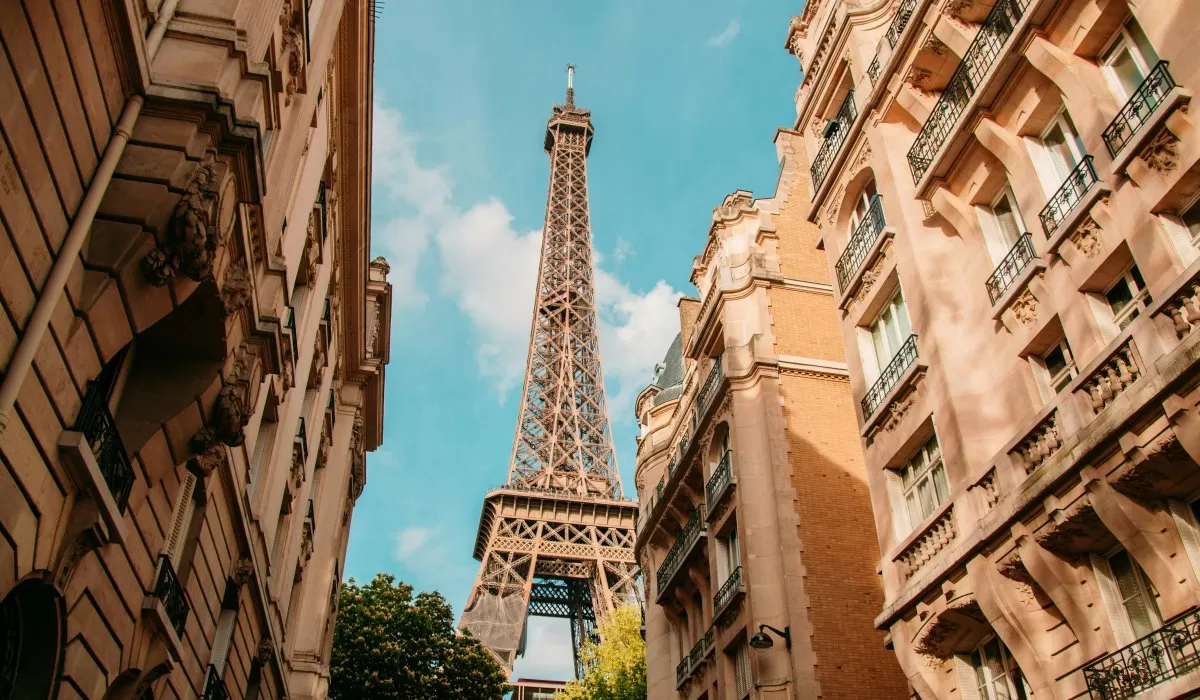 Eiffel Tower between Parisian buildings under a blue sky.
