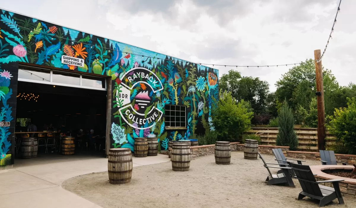 Colorful mural-covered patio with wooden barrels, outdoor seating, and string lights.