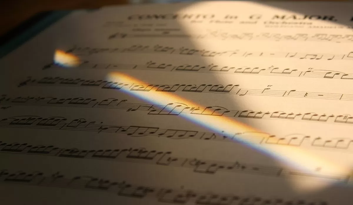 Close-up of handwritten musical notation on sheet music, illuminated by a rainbow of light.