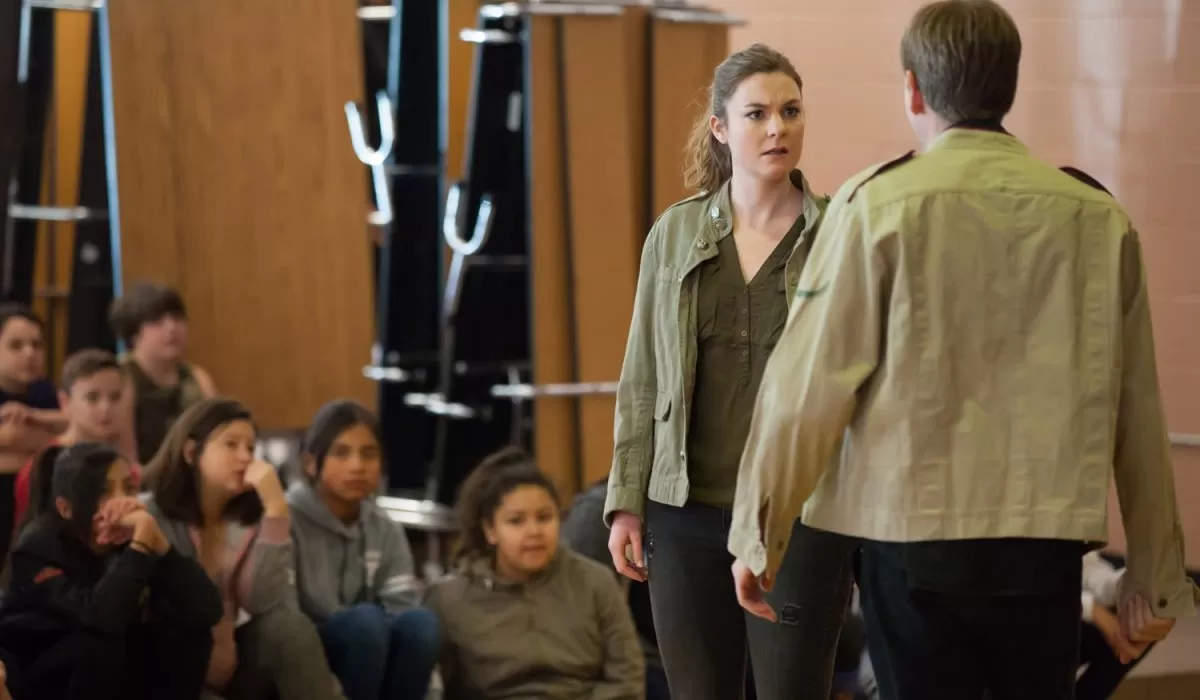 Actors in classroom facing each other while children watch.