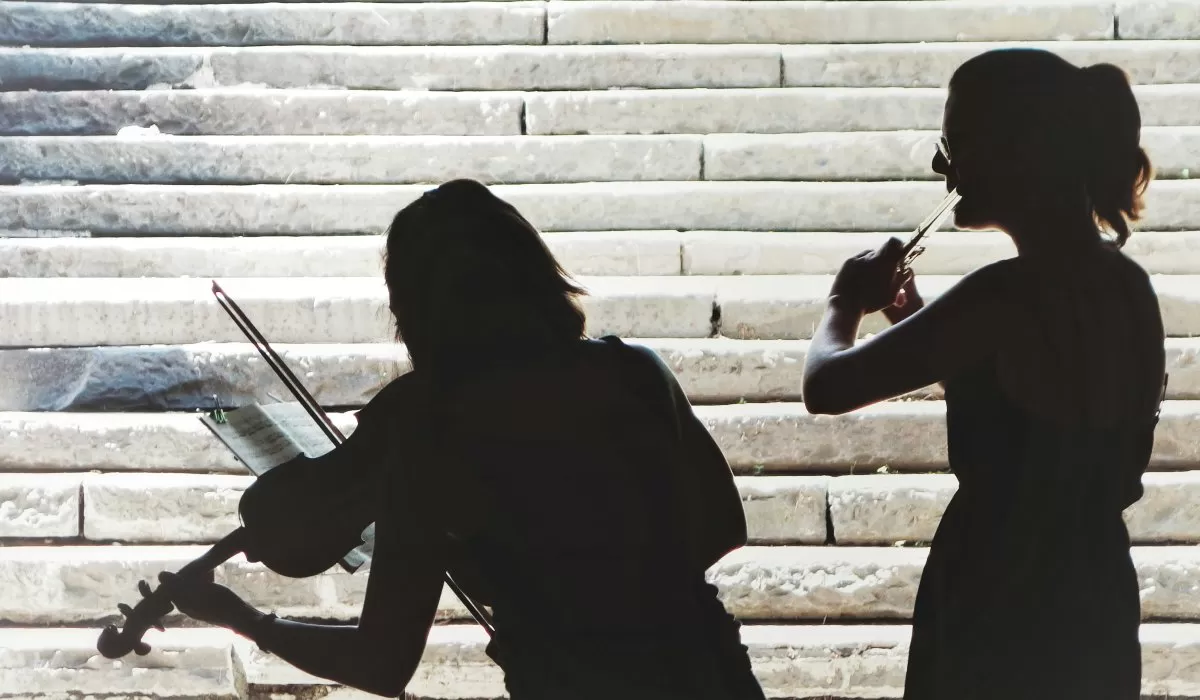 Silhouettes of two violinists playing in front of stone steps.