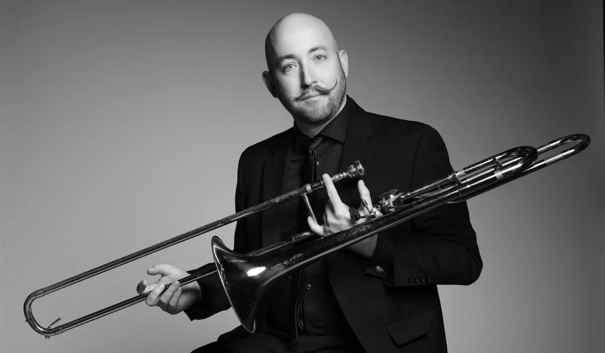 Black-and-white portrait of a musician holding a trombone and smiling at the camera.