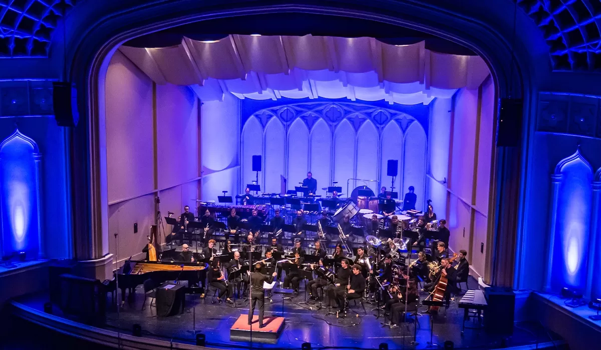 Band orchestra performing on the stage of Macky Auditorium, with a conductor leading musicians