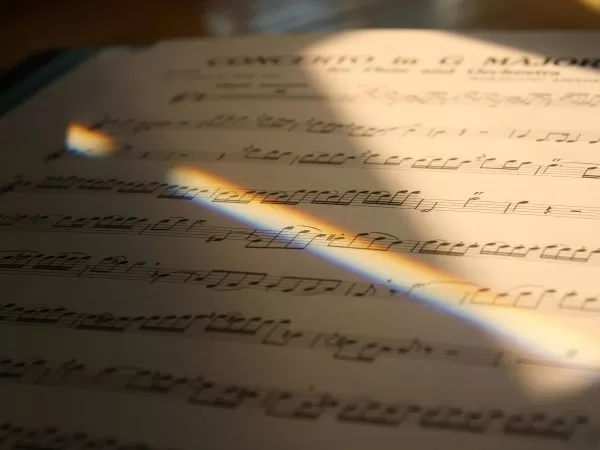 Close-up of handwritten musical notation on sheet music, illuminated by a rainbow of light.