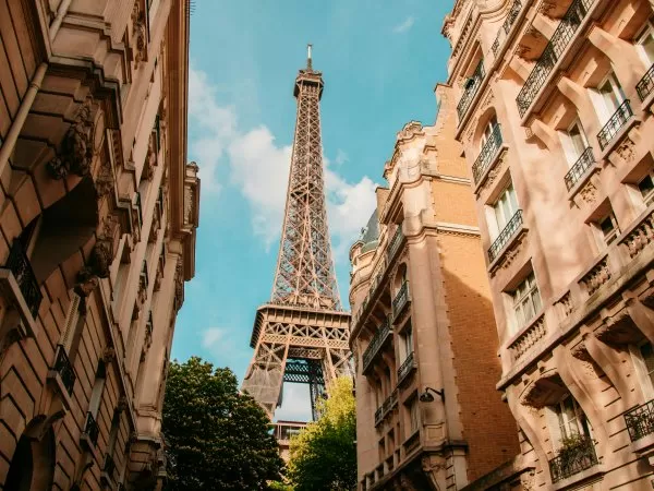 Eiffel Tower between Parisian buildings under a blue sky.