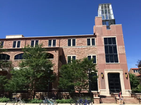 Exterior view of the Atlas building on a sunny day, featuring a stone façade, glass clock tower, trees lining the entrance, and bicycles parked along the sidewalk.