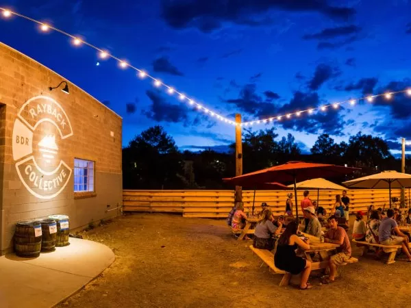Outdoor garden at dusk with picnic tables, umbrellas, and string lights.