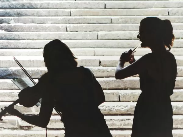 Silhouettes of two violinists playing in front of stone steps.