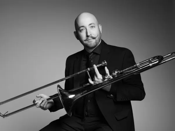Black-and-white portrait of a musician holding a trombone and smiling at the camera.