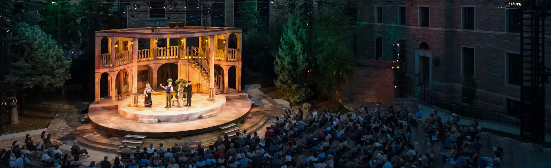 Actors on a stage with an audience in an outdoor theater.